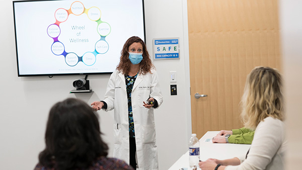 A doctor wearing a mask presenting a slideshow about wellness to a classroom